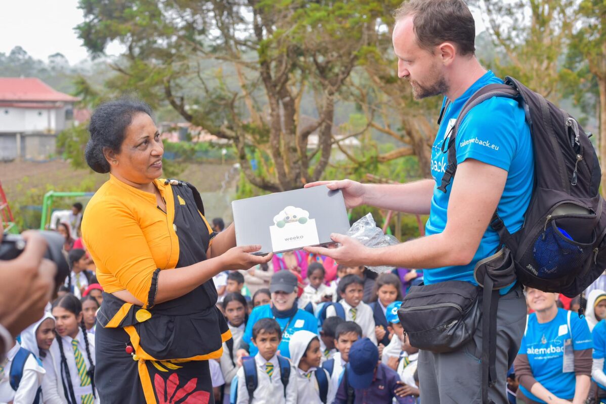 Membro del Gruppo Xera e donna locale dello Sri Lanka sorreggono insieme l'agenda WEEKO durante la missione in Sri Lanka con l'organizzazione no-profit Take Me Back.